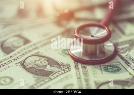 Nahaufnahme des roten Stethoskops auf der US-Dollar-Banknote auf Holztisch. Gesundheitscheck oder Geld- und Finanzkonzept Stockfoto