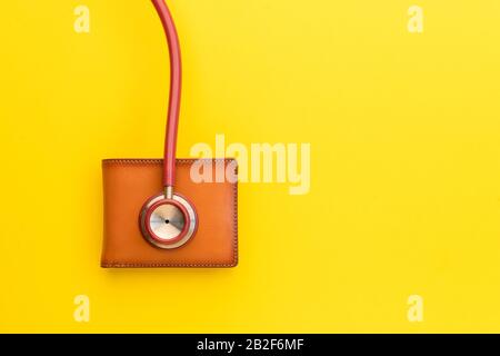 Schließen Sie das Stethoskop des Arztes und die neue lederbraune Männertasche auf gelbem Hintergrund. Budget für Gesundheitscheck oder Geld- und Finanzkonzept Stockfoto