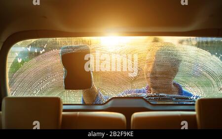 Asiatischer Mann mit blauem Schwamm und Seife zum Waschen des Autos im Freien bei Sonnenuntergang. Konzept für die Reinigung und Wartung von Autos Stockfoto