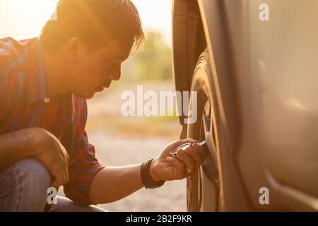 Asian man kontrolliert den Luftdruck und füllt Luft in die Reifen seines Autos. Fahrzeugwartung vor dem Fahrkonzept Stockfoto