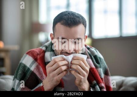 Dunkelhaariger junger kranker Mann niest und fühlt sich schlecht an Stockfoto