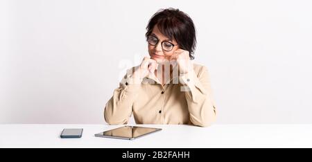 Schöne ältere Frau arbeiten zu Hause in Brillen und bequeme Kleidung per Smartphone und Tablet. Stockfoto