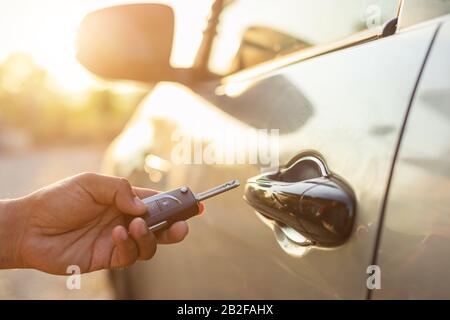 Öffnen Sie das Fahrzeugkonzept: Halten Sie Die Fernbedienungstasten in Der Hand, und drücken Sie die Taste, oder sperren Sie das silberne Auto auf dem Außenparkplatz mit Sonneneinstrahlung in mo Stockfoto