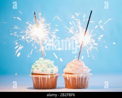 Zwei Cupcakes mit bunten Besprengungen und Glitzern. Festliche Cupcakes mit blauen und rosafarbenen Einsprengseln auf blauem Grund Stockfoto