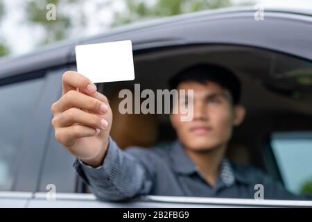 Junger asiat sitzt im modernen Auto und hält keine weiße Karte. Für Mietwagen oder Autogeschäft Stockfoto