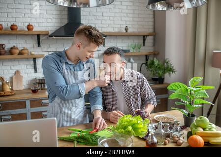 Junger Mann in einer Schürze, die seinen Partner füttert Stockfoto