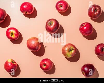 Köstliche rote Äpfel auf orangefarbenem oder korallenrosa Hintergrundmuster. Farbenfroher Obstrahmen. Flaches Lay oder Draufsicht, Hartes Licht. Kreatives Konzept. Stockfoto