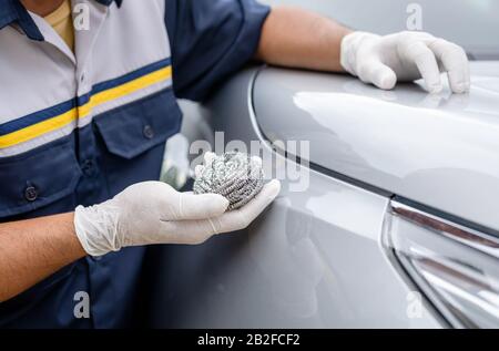 Hand von Menschen, die Edelstahlwolle zum Polieren der Oberfläche der Karosserie verwenden. Falsche Reinigung oder Waschen des Autokonzepts Stockfoto