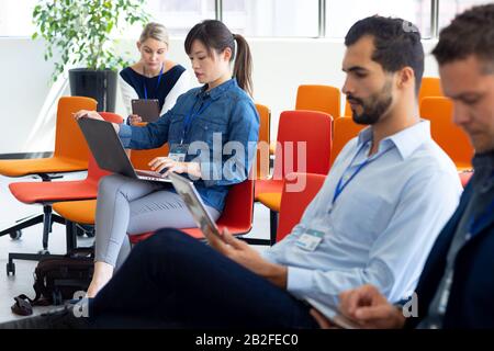 Seitenansicht einer multiethnischen Gruppe von Geschäftsleuten und Geschäftsfrauen, die im Foyer eines modernen Büros arbeiten, sitzen und Laptop und digitaler Tisch benutzen Stockfoto