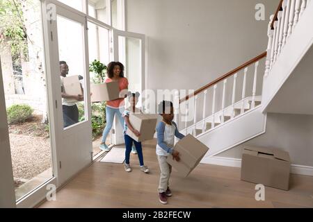 Vorderansicht eines afroamerikanischen Ehepaares mit Sohn und Tochter zu Hause, in ihr Haus einziehen und Pappkartons tragen. Familie genießt Zeit Stockfoto