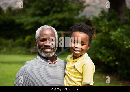 Porträt eines älteren afroamerikanischen Mannes mit seinem Enkel im Garten, Mann mit dem Jungen und lächelnd vor der Kamera. Familie genießt Zeit zu Hause, lif Stockfoto