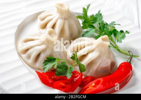 Nahaufnahme einer Portion Khinkali, Knödel mit Fleischfüllung auf einem weißen Teller mit Petersilie und Chili, georgische Küche, horizontaler Blick von Stockfoto