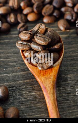 Draufsicht auf Teelöffel aus Holz, gefüllt mit Kaffeebohnen, abgerundet mit Kaffeesamen über dem Woodenhintergrund. Stockfoto