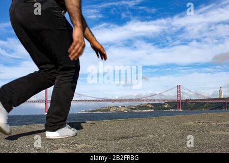 Bild der unteren Hälfte eines Laufers, das an einem Sommertag mit blauem Sk vor der 25-de-Abril-Brücke in Lissabon, Portugal, zu sehen ist Stockfoto