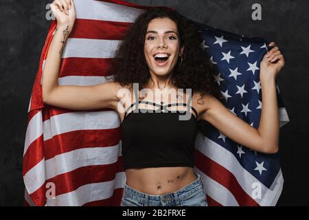 Bild einer jungen kaukasischen Frau mit einem Tattoo, das mit der Kamera lächelt und die amerikanische Flagge über schwarzem Hintergrund isoliert hält Stockfoto