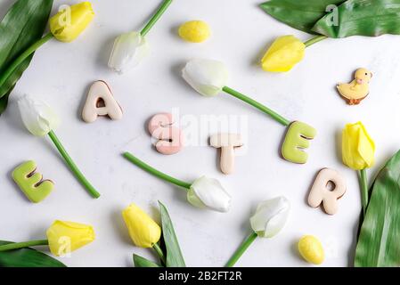 Ostergrüßkarte mit Tulpenblumenmuster, ostereiern und Kaninchenplätzchen. Draufsicht über den weißen Marmortisch Stockfoto