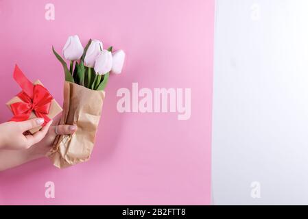 Gratulationskomposition mit weiblichen Händen, die Geschenk-Handkiste und Tulpen-Bouquet gegen duotone bunte Wand halten. Stockfoto