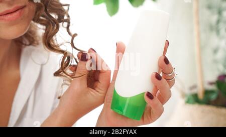 Hübsche Frau mit weißem, leerem Kosmetikschlauch für lockige Haarpflege in der Hand Stockfoto