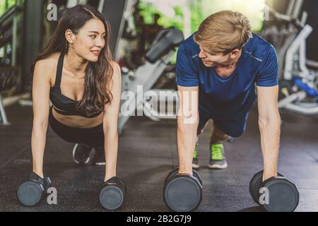 Koppeln Sie die junge Vielfalt, die im Fitness-Sportkomplex des Fitnessstudios arbeitet, trainieren Sie Arme und Kardio, Position der Körperhaltung, schieben Sie die Gewichte hoch, Und Machen Sie Plank Stockfoto