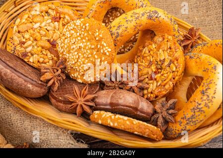 Plätzchen, Schokoladenkuchen und Bagels in einem Korbkorb auf dem Hintergrund rauer Homespun-Qualität. Nahaufnahme Stockfoto