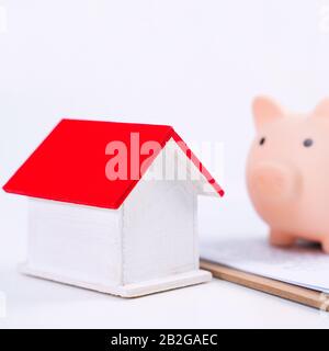 Finanzklage - Piggy Bank, wunderschönes rot-weißes Holzhausmodell auf weißem Hintergrund, spart Geld beim Kauf von Versicherungen, Nahaufnahme, Kopierplatz. Stockfoto