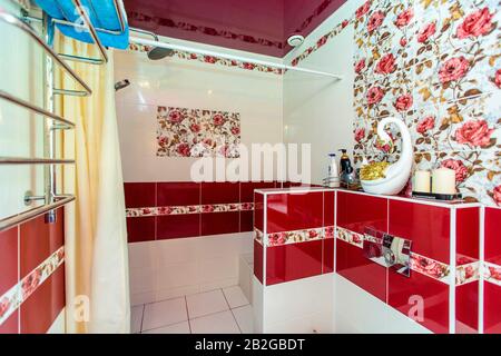 Großes Badezimmer im Cottage in rot-weißen Farben. Kastanienbraune und weiße Fliesen, Fliesen mit roten Farben. Toilette, Dusche. Weiße und kastanienbraune Fliesen auf dem fl Stockfoto