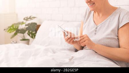 Moderne ältere Dame, die im Internet auf dem Handy im Bett surft Stockfoto