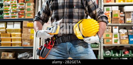 Elektriker hält Multimeter in der Hand, Helm mit Schutzbrille. Bauindustrie, Elektrik. Stockfoto