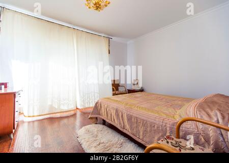 Ein großes Schlafzimmer mit Mahagoni, Korbstühlen und einem eleganten Schminktisch mit einem halbkreisförmigen Spiegel. Das Bett hat eine beige Decke in Quadraten. Stockfoto