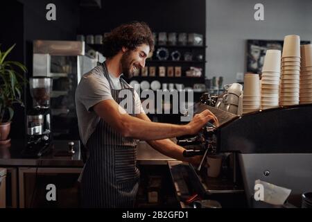 Lächelnder Mann mit Schürze, der Kaffee für den Kunden in seinem kleinen Unternehmen vorbereitet