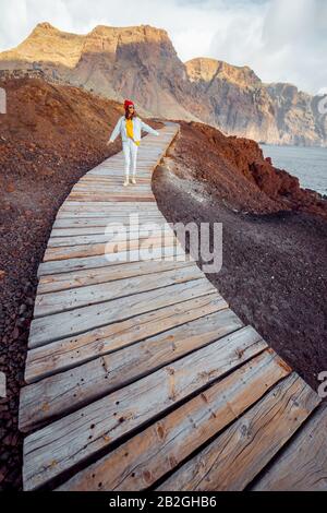 Frau, die auf dem malerischen Holzweg durch das felsige Land mit Bergen auf dem Hintergrund spazieren geht. Reisen auf dem nordwest-kap der Insel Tenera, Spanien Stockfoto