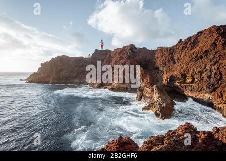 Schöne Landschaft an einer felsigen Küste mit Leuchtturm und gewelltem Ozean bei Sonnenuntergang. TeNo cape im Nordwesten der Insel Tena Stockfoto