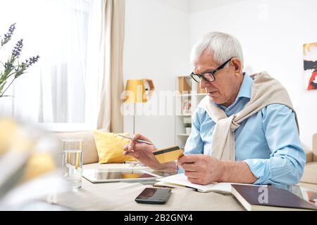 Betagte ältere Menschen knitterten mit einem digitalen Tablet in Brillen, während sie zu Hause den Kontostand der Debitkarte überprüften Stockfoto