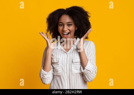 Freudige Afro-Frau, Die Die Hände In Verwunderung Hob Und Mit Einem Lächeln Auf Camera Lächelte Stockfoto