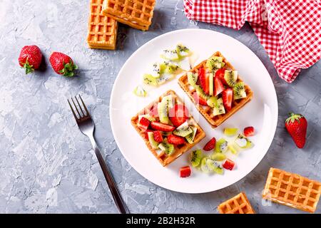 Belgische Waffeln mit Erdbeeren und Kiwi auf weißem Teller Stockfoto