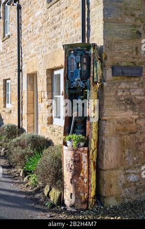 Alte Benzinpumpe vor einem cotswold-steinhäuschen. Withington, Cotswolds, Gloucestershire, England Stockfoto