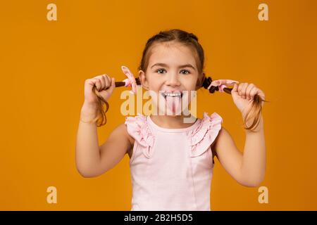 Fröhliches kleines Mädchen, das ihre Zunge auf gelbem Hintergrund zeigt. Gesichtsausdruck Stockfoto