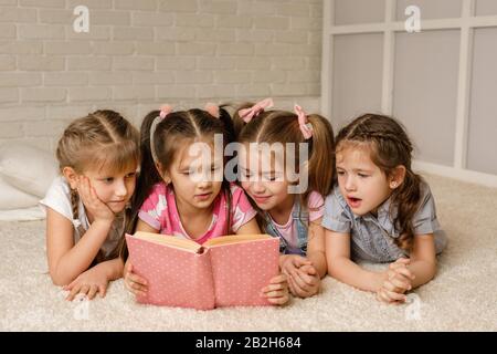 Die Gruppe der Kinder legte sich auf den Boden und las das Märchenbuch. Vier kleine Mädchen studierten zusammen in der Klasse. Freundschaftskonzept Stockfoto