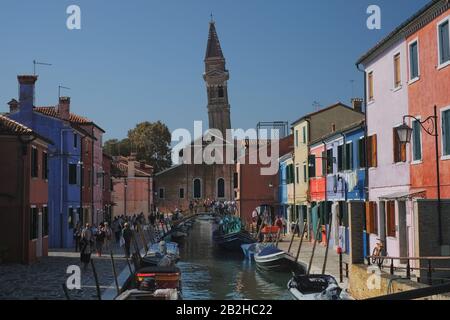 Brücke über Riva dei Santi, vertäute Boote und farbenfrohe Häuser, Parrocchia di San Martino Vescovo und den schiefen Glockenturm von Burano, Venedig Stockfoto