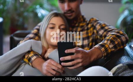 Junges Paar, das auf dem Sofa auf das Telefon blickt Stockfoto
