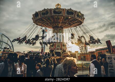 Die Sonne geht über das Oktoberfest in München, mit Hunderten von Menschen in traditionellen Lederhosen und Dirndls. Stockfoto