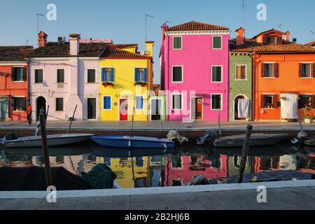 Burano Venedig, farbenfrohe Häuser und Reflexionen, heißes Rosa, Orange, Gelb und Grün am Kanal entlang Fondamenta della Pescheria im Morgenlicht Stockfoto