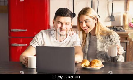 Schönes junges Paar mit Frühstück und Laptop am Tisch in der Küche Stockfoto