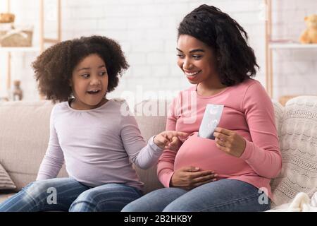 Schwangere Afro-Mutter zeigt ihrer kleinen Tochter Ultraschall-Scan-Foto Stockfoto