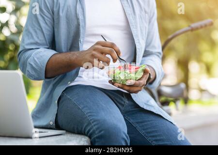 Unerkennbarer Afrikanischer Mann, Der Salat Isst Und Im Park Gesundes Mittagessen Im Freien Hat Stockfoto