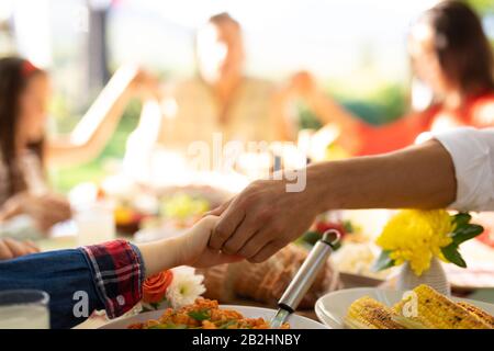 Nahaufnahme der Hände eines kaukasischen Vaters und Sohnes, der draußen an einem Esstisch sitzt, der für eine Mahlzeit eingerichtet ist, die Familie, die alle Hände im Gebet hält, konzentriert sich auf Stockfoto