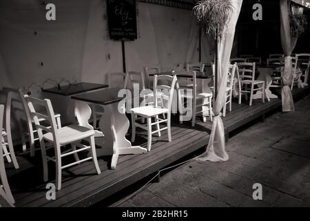 Weiße Stühle und Tische auf einem Holzdeck auf der Straße, eine Trattoria nach der Schließung in der Nacht, keine Menschen, ein urbanes Stillleben in Monterosso Stockfoto