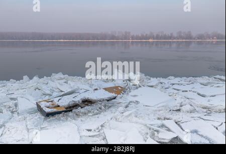 Zerstörtes Boot auf einem gefrorenen Donau-Fluss mit fantastischem Sonnenuntergang in der Nähe von Belgrad, Zemun, Serbien Stockfoto