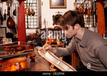 Lustiger Geigenbauer, der in einer Werkstatt an der Herstellung einer Geige arbeitet Stockfoto