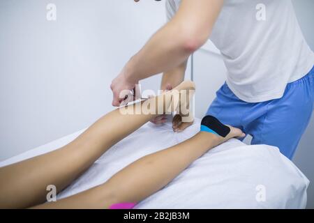 Ein Physiotherapeut ist Kinesio Tape auf Bein des Patienten anwenden. Stockfoto